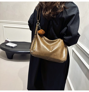 Detail of a brown leather shoulder bag with a plush bear charm and woven tassel details