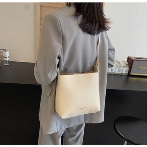Détail du sac seau minimaliste en cuir crème avec lettrage doré et bandoulière réglable