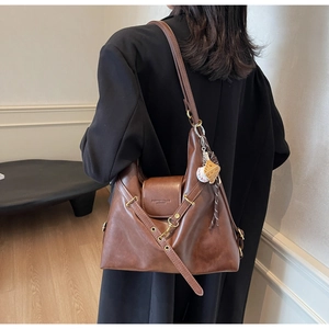 Detalle de un bolso tote de cuero marrón grande con correa y colgante de béisbol