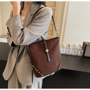 Detail view of large dark brown suede bucket bag with gold rivets on female model
