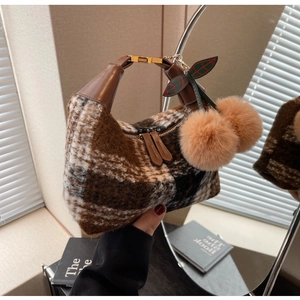 Detaillierte Makroansicht des braun karierten Plüschstoffs und Kirsch-Pompons der Hobo-Tasche