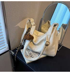 Detail of off-white faux leather hobo bag with teddy bear charm and braided tassel trim