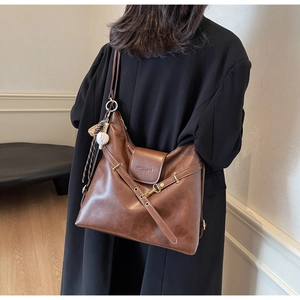 Detalle de bolso tote vintage de cuero marrón con colgante de béisbol y hebillas