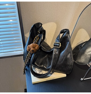 Close-up of black soft leather hobo bag with teddy bear charm on books in soft light
