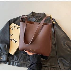 Gros plan d'un sac seau en cuir marron avec lettrage doré sur un fond sombre chic