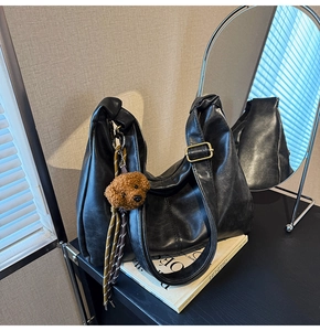 Detail of black faux leather hobo bag with teddy bear charm on art book background