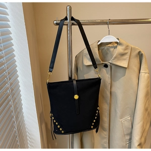 Detail of black bucket bag with gold rivets and leather strap on a trench coat background