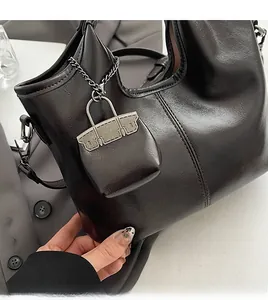 Dettaglio di una borsa tote in pelle lucida scura con mini pochette e catena in metallo
