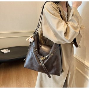Detalle de bolso tote de cuero marrón oscuro con herrajes dorados y adorno de béisbol