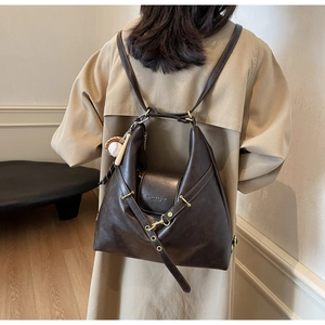 Detalle de una mochila vintage de cuero marrón oscuro con amuleto de béisbol y ojales