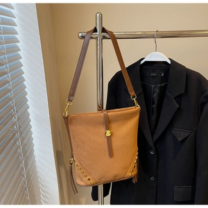 Close-up of a large dark brown suede bucket bag featuring a gold buckle and fringe detail