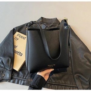Détail du sac seau en cuir noir avec inscription dorée et boucles métalliques dorées