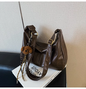 Detail of dark brown leather hobo bag with teddy bear charm and gold metal buckle