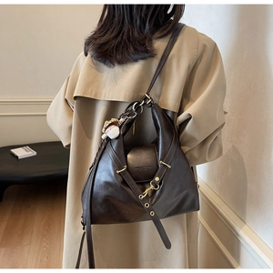 Detalle de bolso tote de cuero marrón oscuro con correas cruzadas y colgante de béisbol