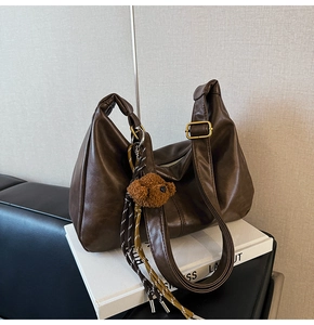 Detail of dark brown hobo bag featuring golden buckle and brown teddy bear charm