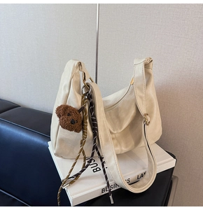 Detail of beige shoulder bag with adjustable strap and cute brown bear pendant