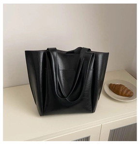 Close-up of a large black faux leather tote bag with glossy finish on a cream surface