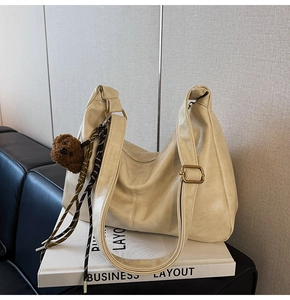 Macro shot of beige hobo bag detail with plush bear charm and adjustable strap