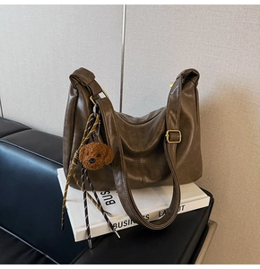Close-up of deep brown soft leather dumpling bag with golden buckle and plush charm