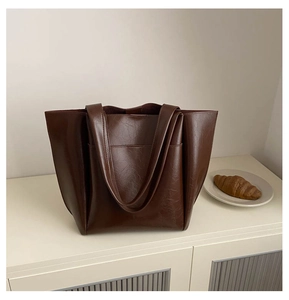 Close-up of a large dark brown tote bag featuring oily faux leather texture and outer pocket