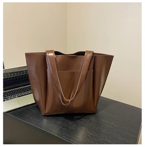 Detail view of large dark brown tote bag with oil wax leather texture on an office desk