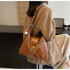 Detalle de bolso tote de cuero marrón con hebilla lateral y adorno de béisbol