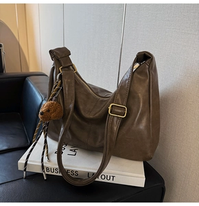 Close-up of matte dark brown pleated leather shoulder bag with bear plush charm