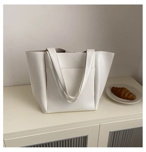 Detail shot of a large white PU leather tote bag featuring a front pocket and side wings