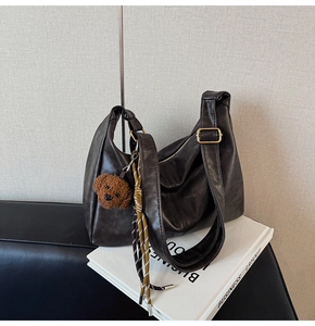 Detail of dark brown PU leather hobo bag with gold buckle and plush bear charm