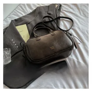 Detail of dark brown leather handbag featuring metal logo, top handles and shoulder strap