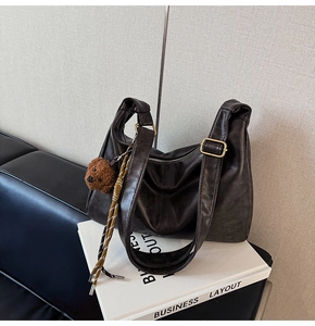 Detail of dark brown leather tote bag featuring a cute plush bear charm and golden buckle strap