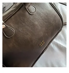Detailed view of the dark textured leather material and golden logo on the square handbag