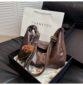Detail of dark brown dumpling bag with metal buckle and plush bear pendant accessory