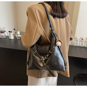 Detalle del bolso tote de cuero negro brillante con colgante de béisbol y correa cruzada