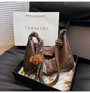 Brown vintage hobo bag with plush dog charm in gift box, featuring soft leather details