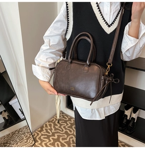 Detail of dark brown retro leather square bag with dual handles and gold metallic logo