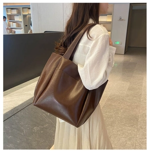 Deep brown oversized tote bag in polished PU leather shown on shoulder for scale