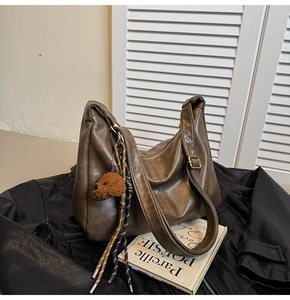 Brown vintage leather dumpling bag with plush dog charm on a leather jacket background