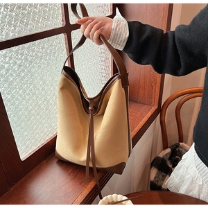 Close-up of mustard suede bucket bag with brown leather trim and drawstring detail