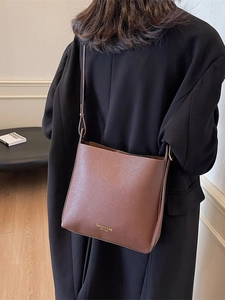 Sac seau en cuir marron avec lettrage doré sur mannequin pour un style de mode haut de gamme