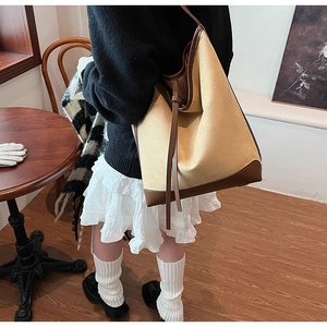 Detail of canvas bucket bag with brown leather trim and side strap accents
