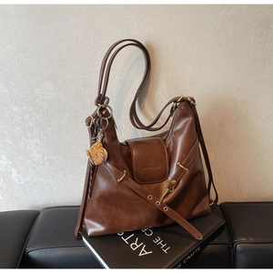 Detalle del bolso tote vintage de cuero marrón con herrajes de latón y amuleto de gato