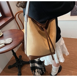 Detail of a large color-block canvas tote bag with brown leather trim and drawstring closure