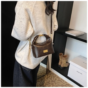 Model showing dark brown leather handbag with gold metal clasp and detachable strap