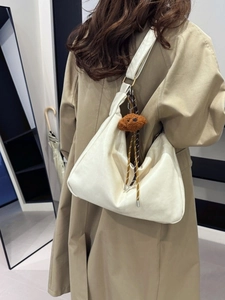 Minimalist beige Hobo shoulder bag with plush bear charm worn by a model in a trench coat