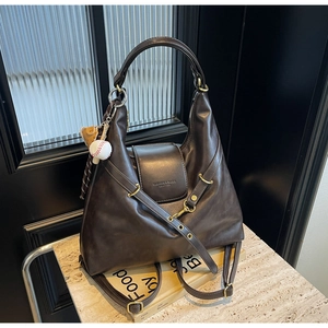 Detalle del bolso tote de cuero café oscuro con relieve y un colgante de béisbol