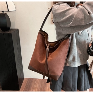 Detail view of large brown suede bucket bag with leather reinforced base and drawstring