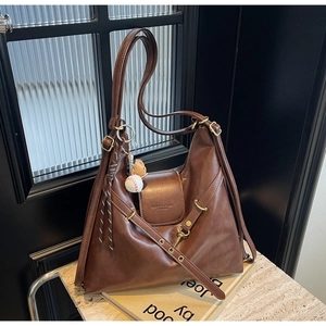 Detalle de bolso hobo de cuero mate marrón oscuro con herrajes dorados y colgante de béisbol