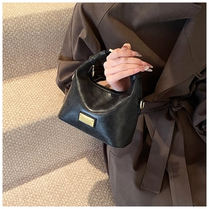 Detailed view of black faux leather half-moon bag featuring premium gold-tone metal logo plate