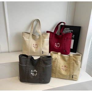 Dettaglio di grandi borse tote in tela in quattro colori con ricami e tasche laterali